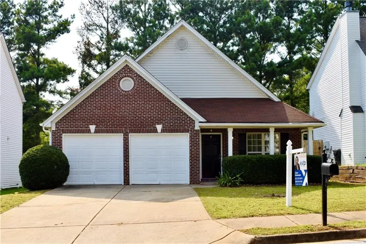 Brick facade home featuring a two-car garage, covered porch entry, and mature landscaping