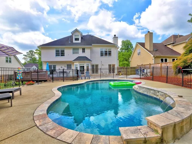 Curved in-ground pool with a stone waterfall feature