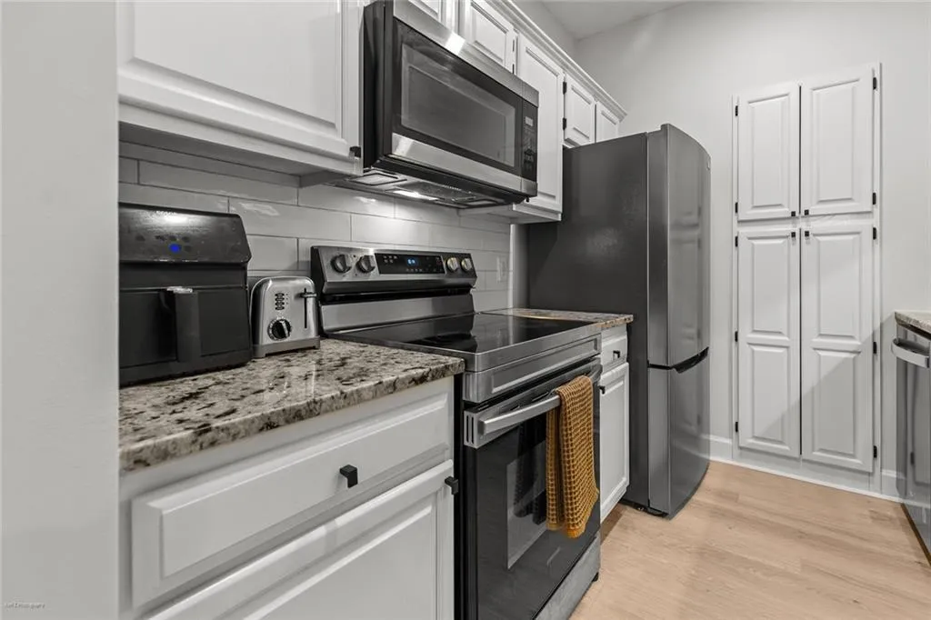 Kitchen with stainless steel appliances, decorative backsplash, white cabinetry, light wood finished floors, and light stone countertops