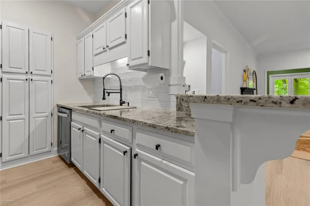 Kitchen with white cabinetry, light wood-style flooring, backsplash, light stone countertops, and stainless steel dishwasher