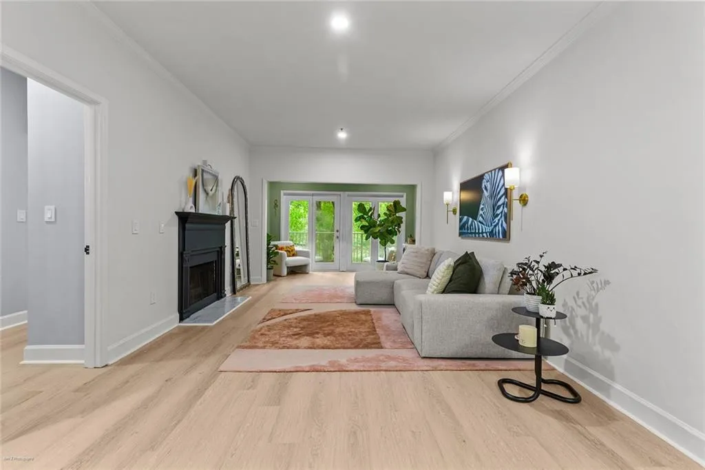 Living room featuring a fireplace with raised hearth, crown molding, light wood-type flooring, and french doors