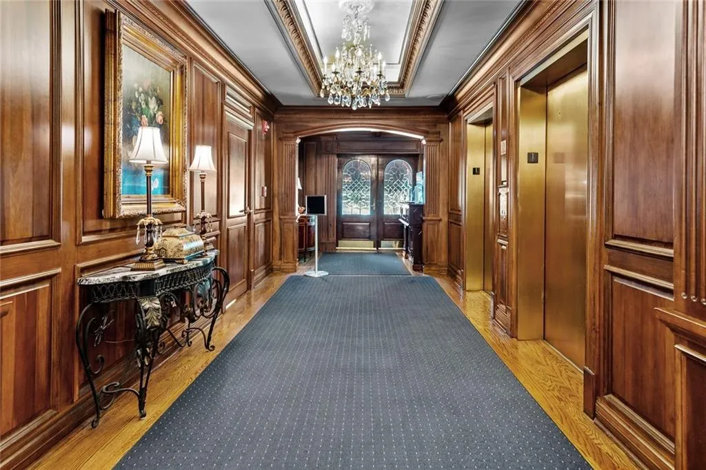 Hall featuring a chandelier, light wood-type flooring, elevator, wood walls, and arched walkways