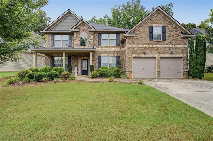 Brick and siding exterior featuring a covered porch with columns, a two-car garage, and established front landscaping