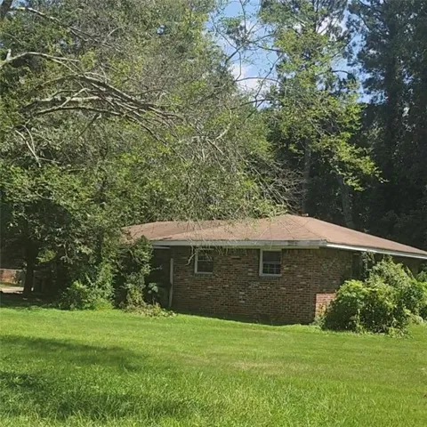 Brick exterior with multiple windows, a brown shingle roof, and a surrounding green lawn