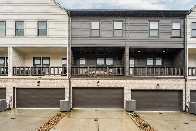 Back of house with a balcony, a garage, driveway, and brick siding