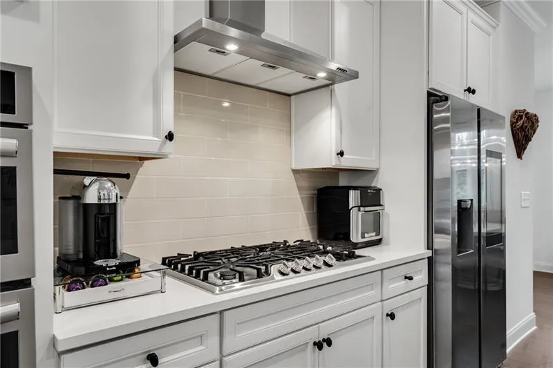 Kitchen featuring white cabinetry, appliances with stainless steel finishes, wall chimney range hood, backsplash, and wood finished floors