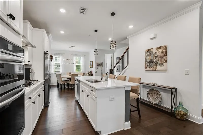 Kitchen featuring white cabinetry, hanging light fixtures, a breakfast bar area, stainless steel appliances, and dark wood-style floors