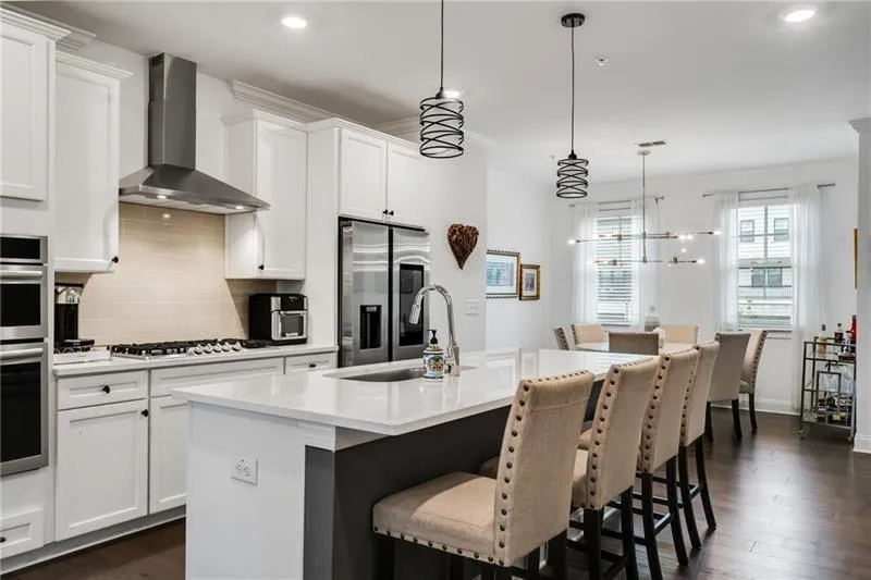 Kitchen with tasteful backsplash, dark wood finished floors, white cabinetry, a breakfast bar, and wall chimney exhaust hood