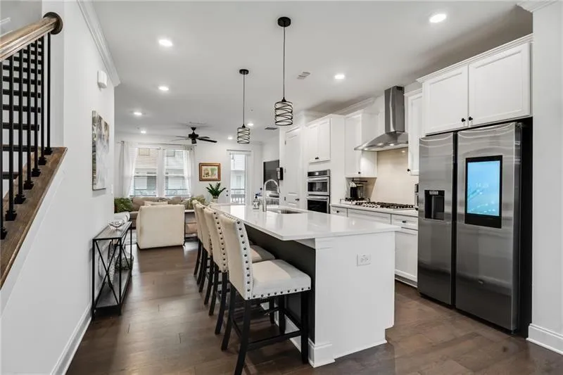 Kitchen with appliances with stainless steel finishes, a kitchen island with sink, decorative light fixtures, dark wood-style flooring, and white cabinetry