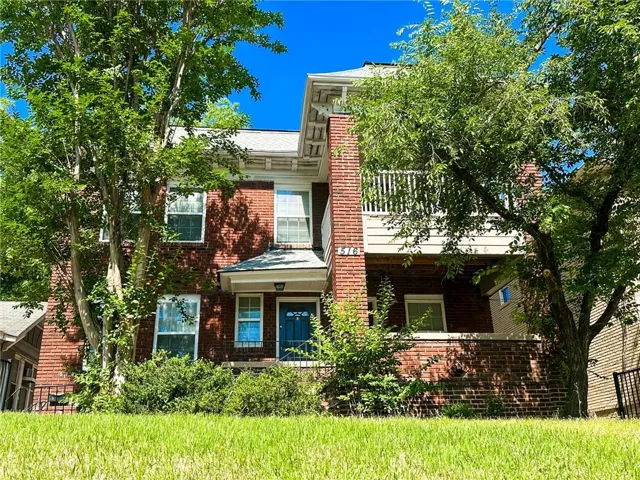 Brick exterior featuring multiple windows, a covered front entry, and a second-story balcony with white railings