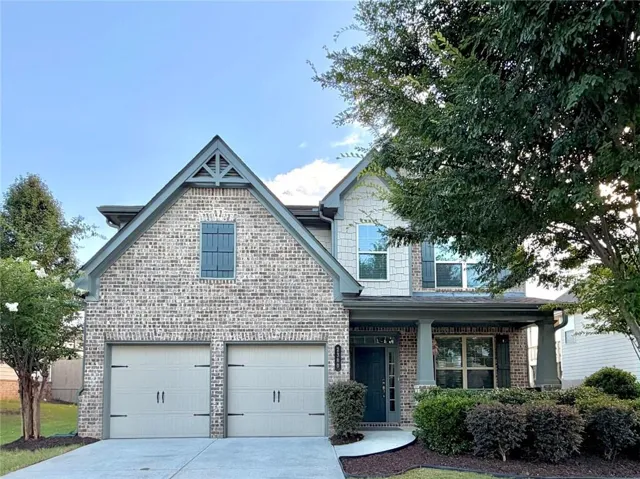 Brick and siding exterior featuring a covered front entry with columns, a two-car garage with decorative hardware, an arched gable vent, and mature landscaping