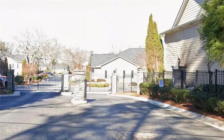 Gated community entrance with stone pillars, wrought iron fencing, and mature landscaping