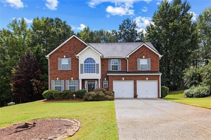 Brick exterior with white trim and gray shutters, featuring a two-car garage, arched window, and established landscaping