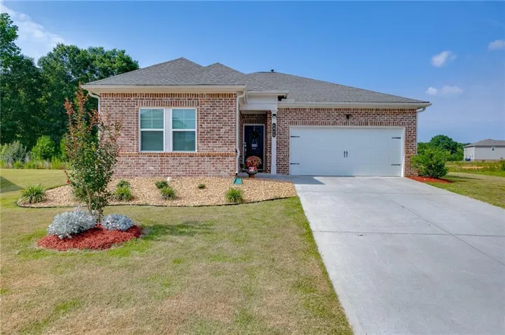 Brick exterior with a gabled roofline, featuring an attached two-car garage, concrete driveway, and landscaped front yard with planting beds