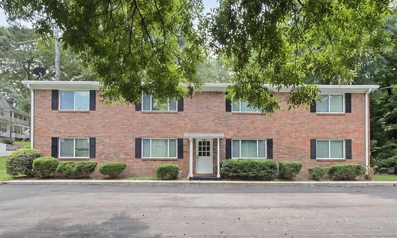 Brick exterior with white trim, black window shutters, a central entrance with a portico, and established foundation plantings