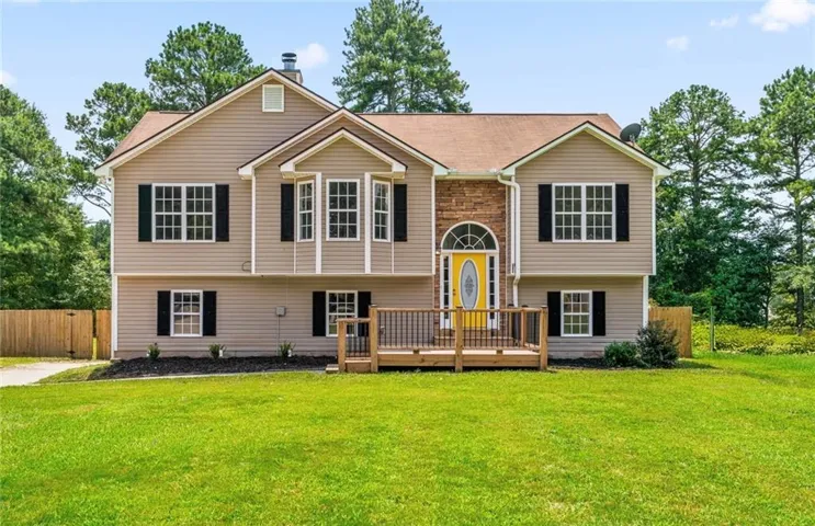 Two-story residence featuring a wood-finish deck, stone veneer accents, and a vibrant yellow entry door