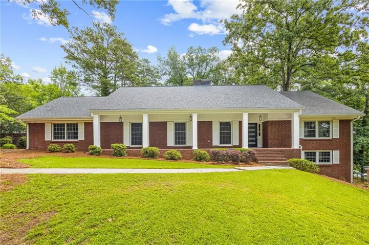 Brick exterior featuring a covered entry porch with white columns, a dark front door, and multiple windows with white shutters