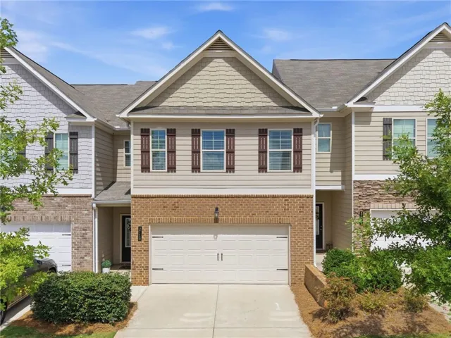 Townhome exterior featuring a two-car garage, brick facade, horizontal siding, decorative shutters, and gabled rooflines