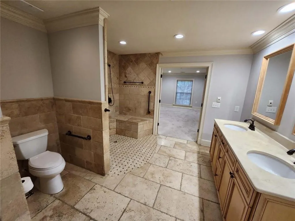 Bathroom featuring crown molding, tiled shower, recessed lighting, double vanity, and stone tile floors