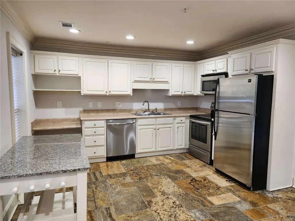 Kitchen with stainless steel appliances, ornamental molding, white cabinetry, dark stone finish flooring, and recessed lighting
