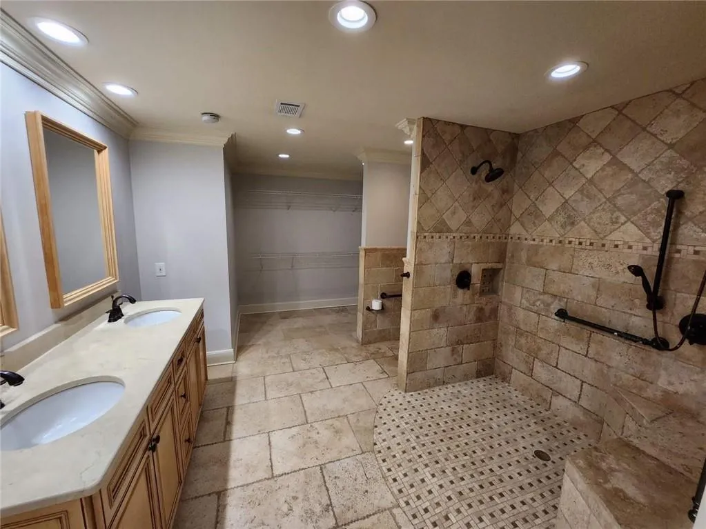 Bathroom with a tile shower, recessed lighting, ornamental molding, double vanity, and stone tile floors