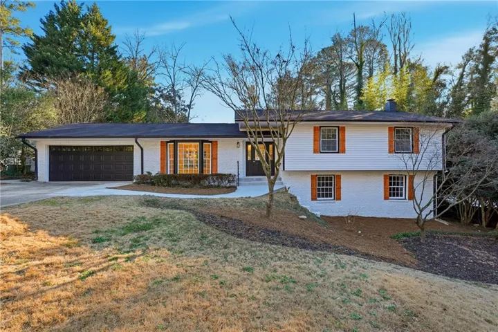 Tri-level home featuring brick siding, concrete driveway, an attached garage, and a chimney