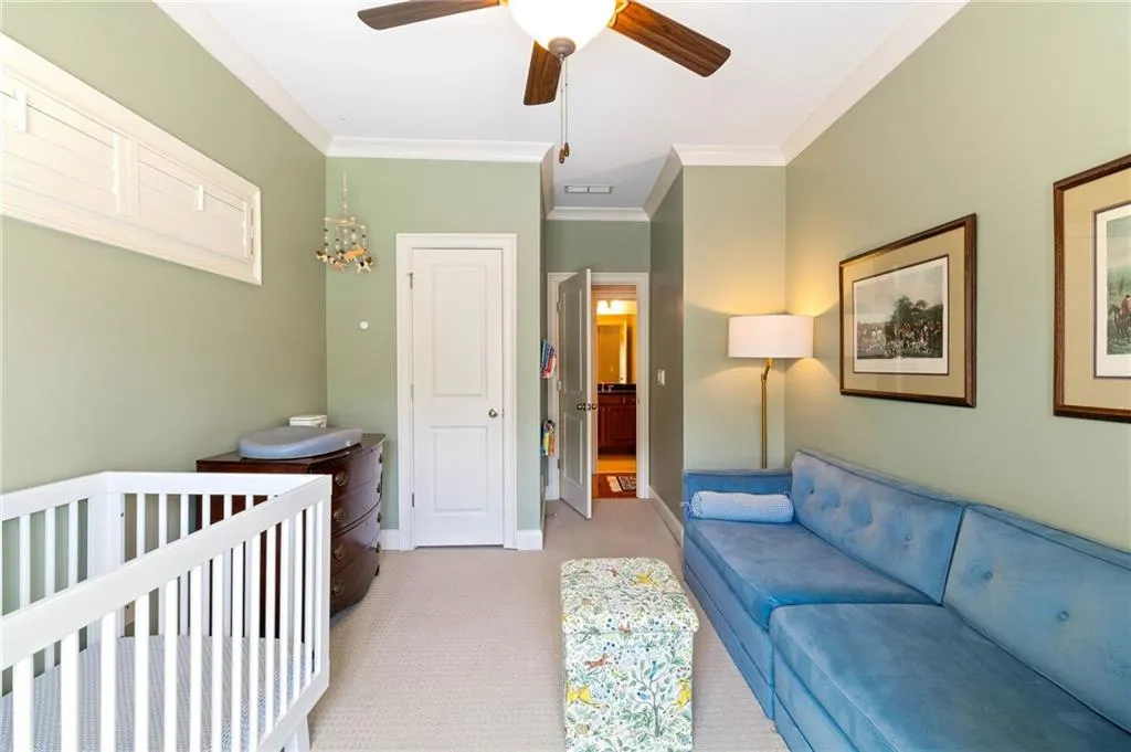 Bedroom featuring ornamental molding, light carpet, a nursery area, and ceiling fan