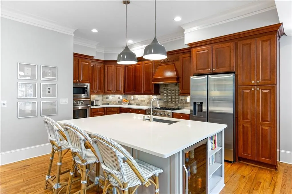 Kitchen with custom exhaust hood, light hardwood / wood-style floors, stainless steel appliances, a kitchen island with sink, and ornamental molding