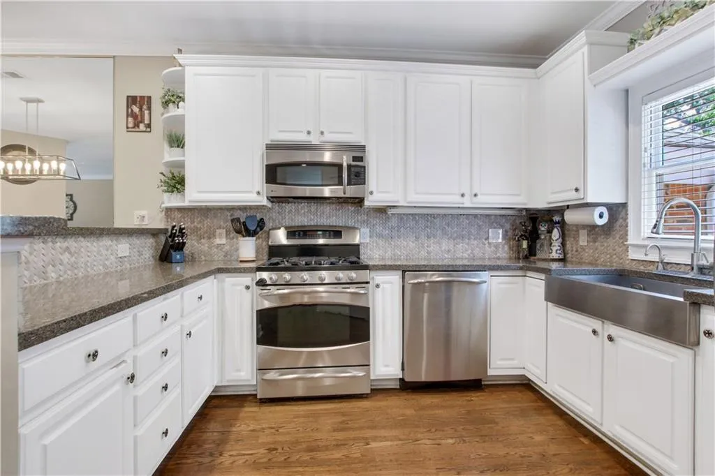 Kitchen with appliances with stainless steel finishes, white cabinets, sink, decorative backsplash, and dark wood-type flooring
