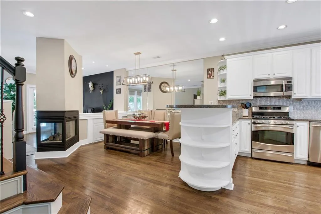 Kitchen with hardwood / wood-style flooring, decorative backsplash, a multi sided fireplace, appliances with stainless steel finishes, and kitchen peninsula