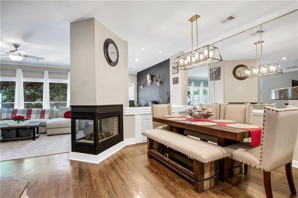 Dining room featuring ceiling fan with notable chandelier, a multi sided fireplace, and hardwood / wood-style flooring