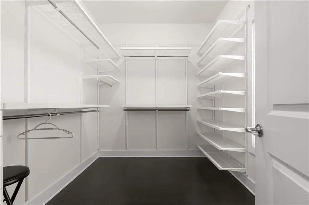 Walk-in closet featuring white wire shelving, multiple hanging rods, dark flooring, and white trim