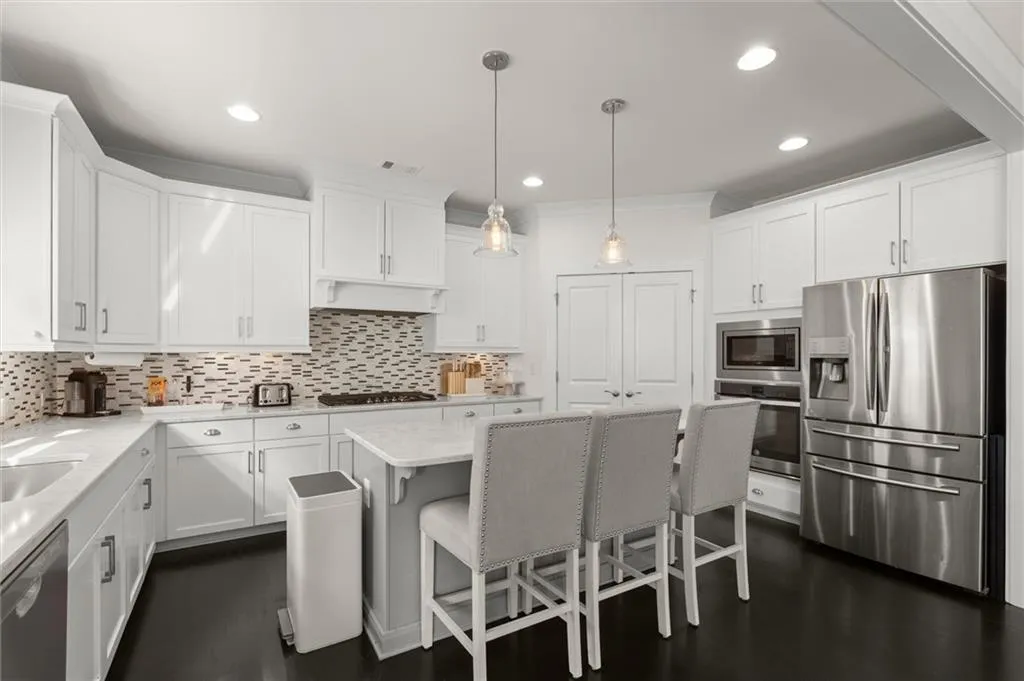 White shaker-style cabinetry, stainless steel appliances, mosaic tile backsplash, central island with seating, and dark wood-finish flooring