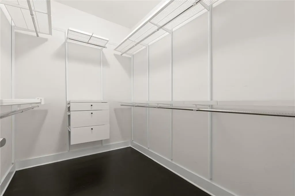 Custom closet system with wire shelving, integrated hanging rods, white cabinetry with three drawers, and dark-finish flooring