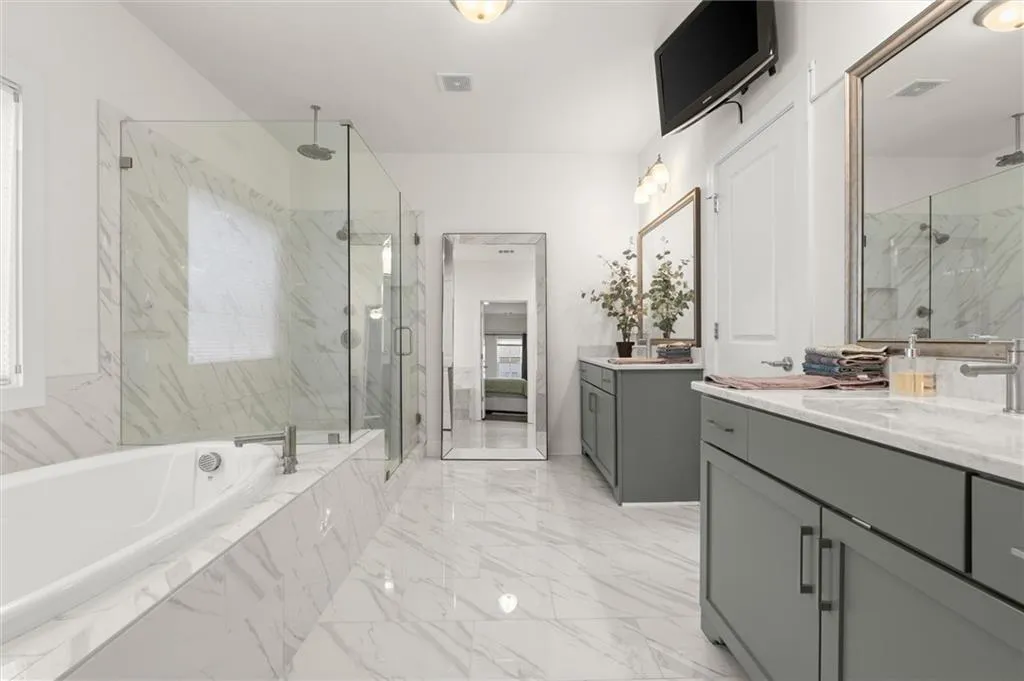 White marble-finish tile flooring, recessed bathtub with deck-mounted faucet, and glass-enclosed shower with multiple showerheads