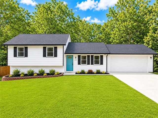 White exterior siding with black shutters, a vibrant blue front door, an attached two-car garage, and a concrete driveway