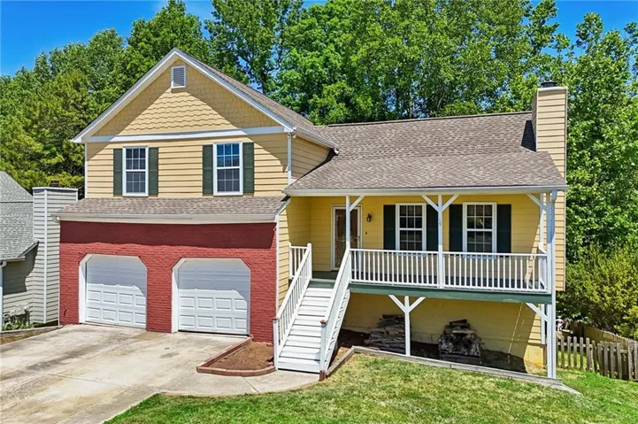 Two-story residence featuring a covered front porch with white railing, a two-car garage with white doors, and a combination of yellow siding and red brick accents
