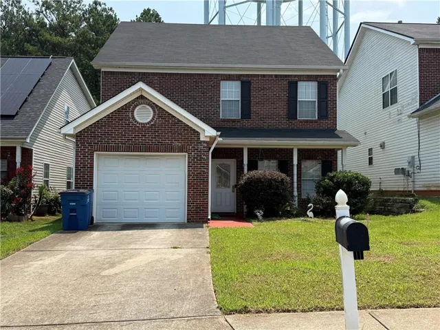Brick exterior featuring white trim, an attached garage, and a covered front entry