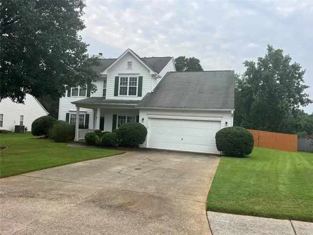 White two-story residence featuring a covered front porch, a two-car garage, and green shutters