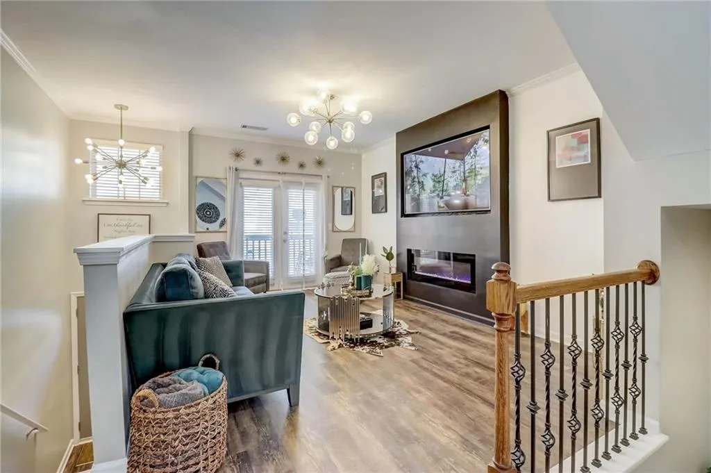 Living area with a chandelier, wood finished floors, ornamental molding, a glass covered fireplace, and french doors