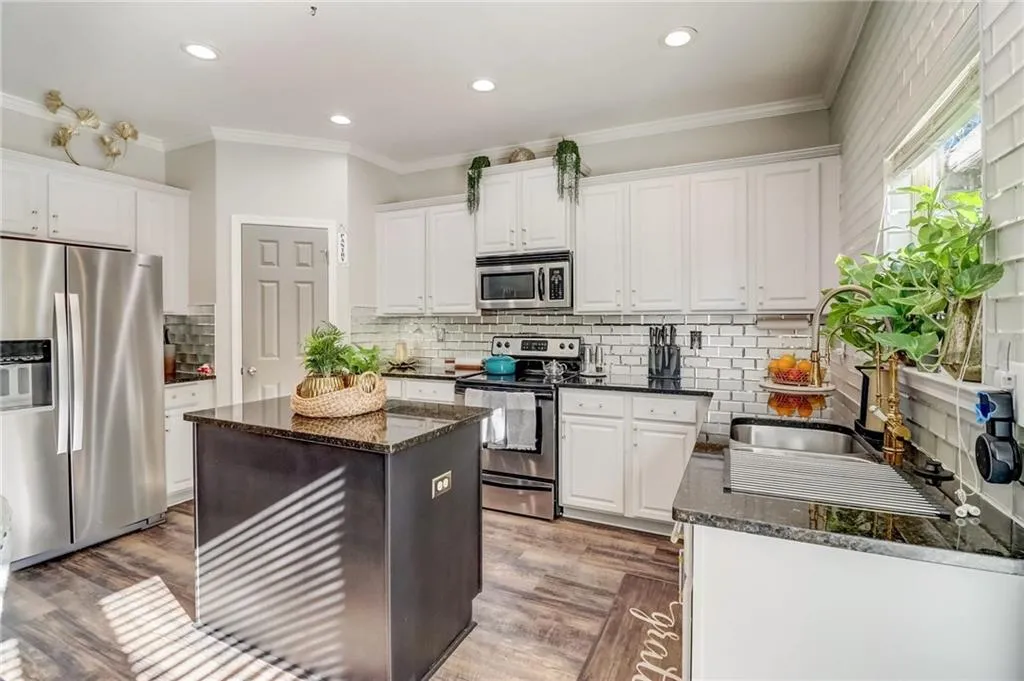 Kitchen with stainless steel appliances, white cabinetry, light wood-type flooring, dark stone counters, and crown molding