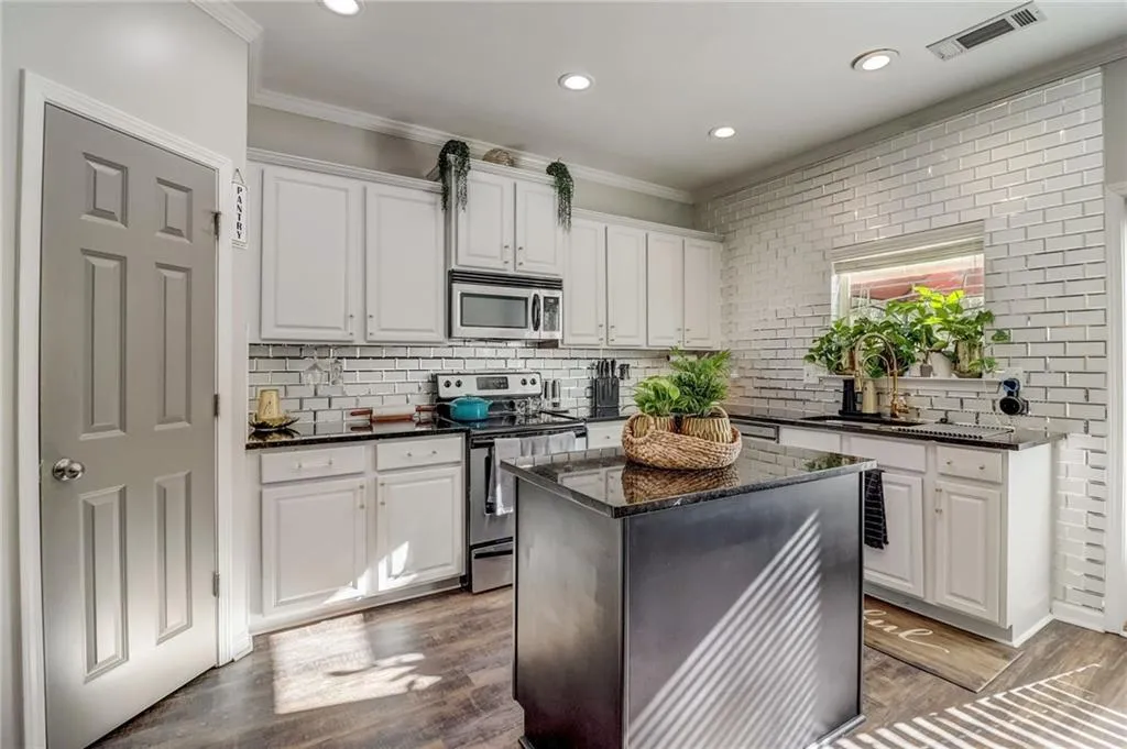 Kitchen featuring stainless steel appliances, white cabinets, dark wood-type flooring, ornamental molding, and dark stone countertops