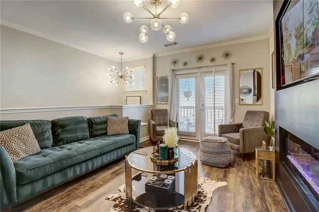 Living area with suspended lighting, ornamental molding, a glass covered fireplace, and wood finished floors