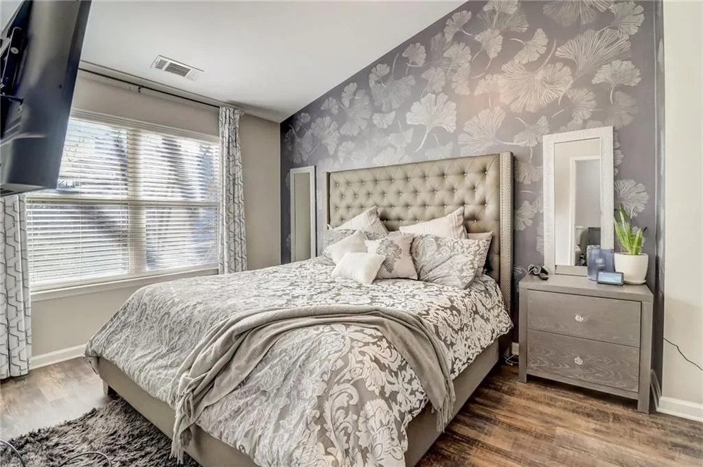 Bedroom with wallpapered walls, wood finished floors, and an accent wall