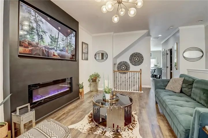 Living room with wood finished floors, ornamental molding, suspended lighting, and a glass covered fireplace