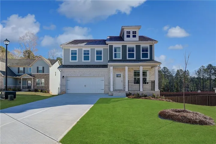 Contemporary two-story residence featuring a two-car garage, stone and siding exterior, front porch with columns, black metal railing, and a manicured green lawn