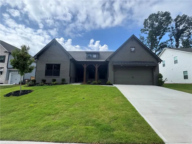 Contemporary gray brick facade featuring a covered entry porch with wood columns, a two-car garage with a metal awning, a neatly manicured lawn, and a concrete driveway