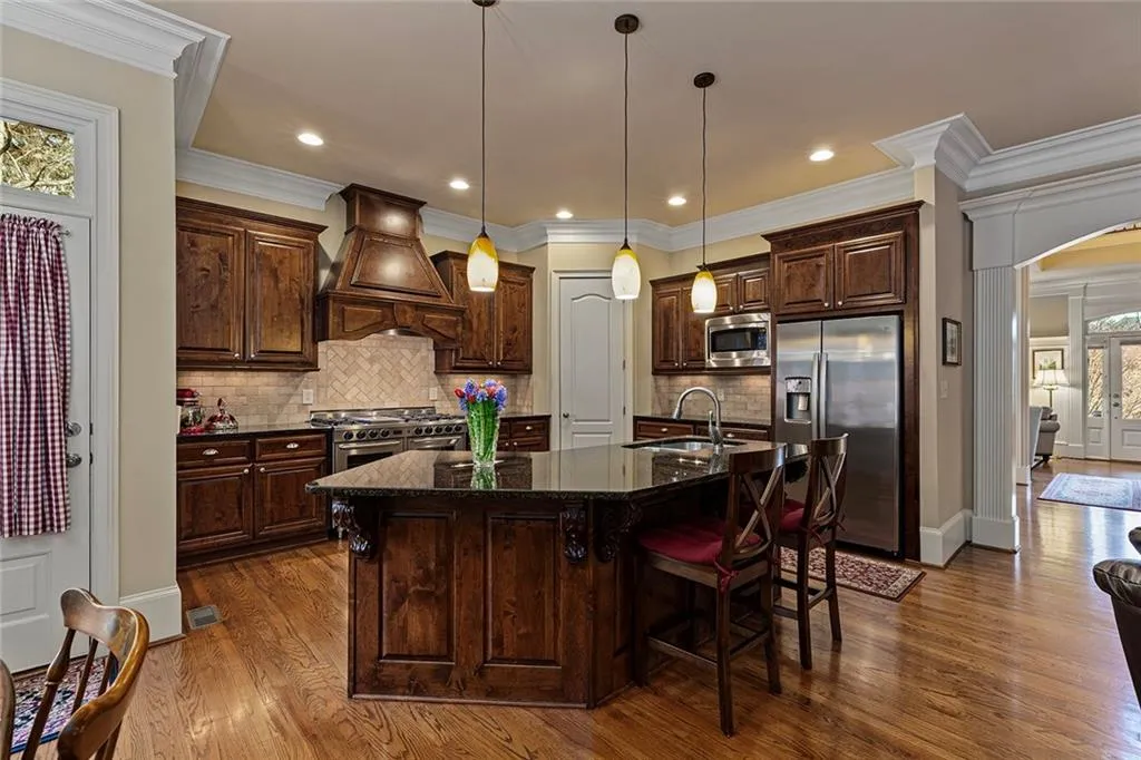 Kitchen with decorative light fixtures, sink, stainless steel appliances, custom range hood, and a center island with sink