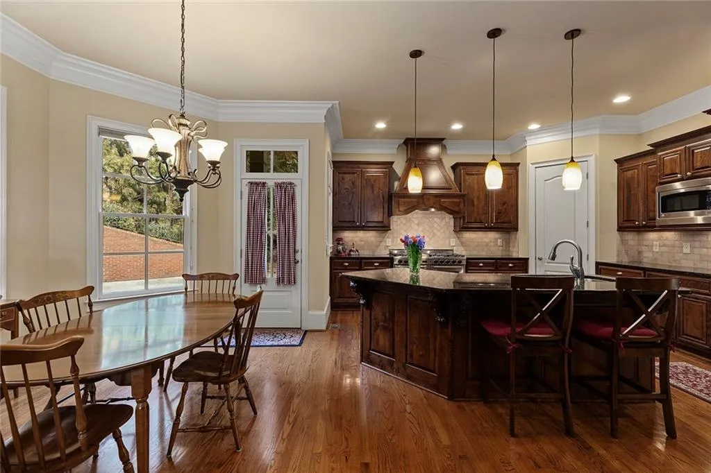 Kitchen featuring appliances with stainless steel finishes, a kitchen breakfast bar, an island with sink, decorative light fixtures, and custom exhaust hood
