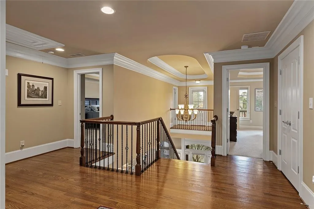 Hall with an inviting chandelier, hardwood / wood-style flooring, ornamental molding, and a raised ceiling
